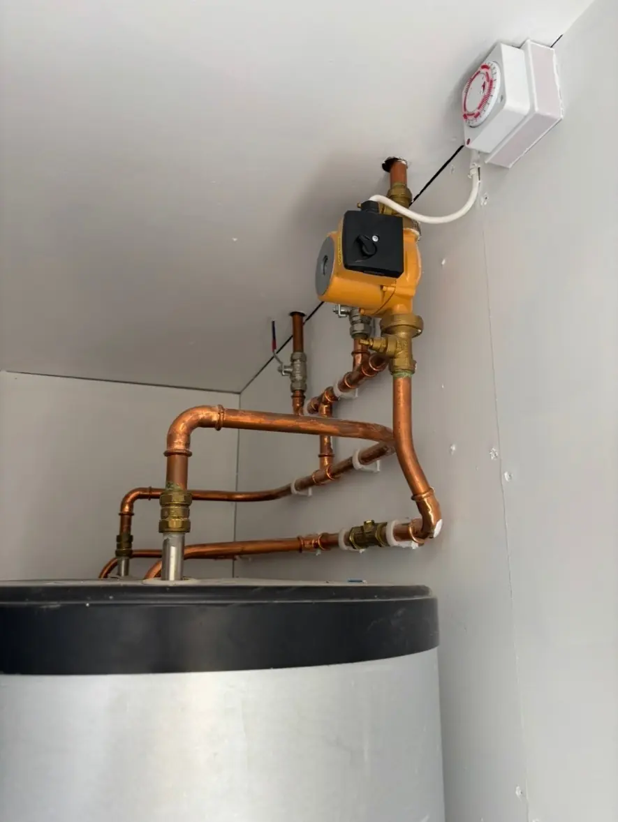 Top of a hot water cylinder with copper pipework and heating controls fitted above it